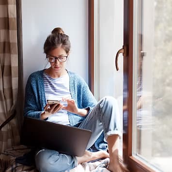 A woman reviewing her health information on a laptop by a window