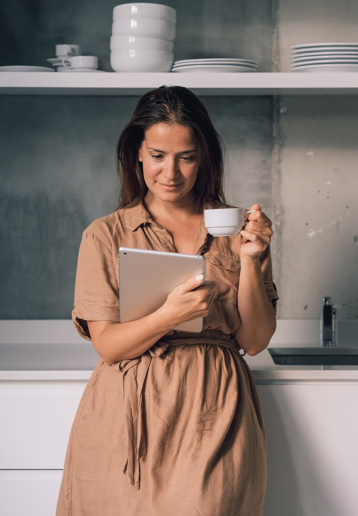 A woman holding a tablet and a cup, engaged with her health plan at home